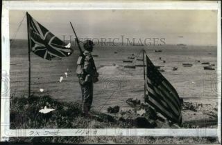 1943 Press Photo Soldier Stands Between Us & Canadian Flags,  Kiska Island